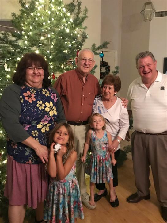 Family members pose happily together in front of a large Christmas tree adorned with lights.