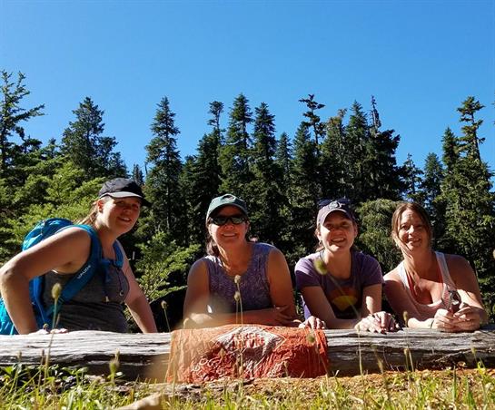 Friends gather outdoors, smiling and enjoying each other's company in a lush forest setting.