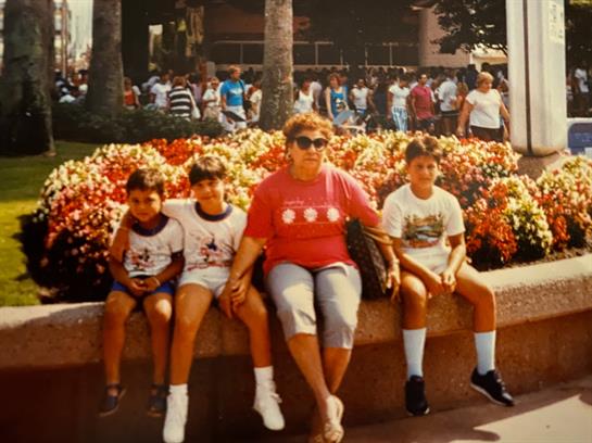 Four people relax near vibrant flowers with crowds in the background, capturing a joyful moment.