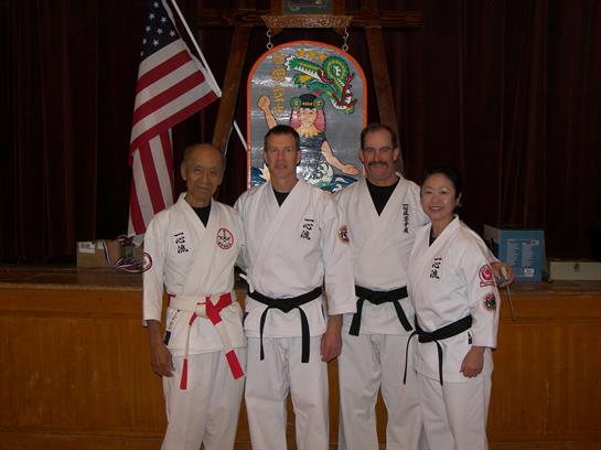 Four martial artists in traditional uniforms showcase their skills and unity.