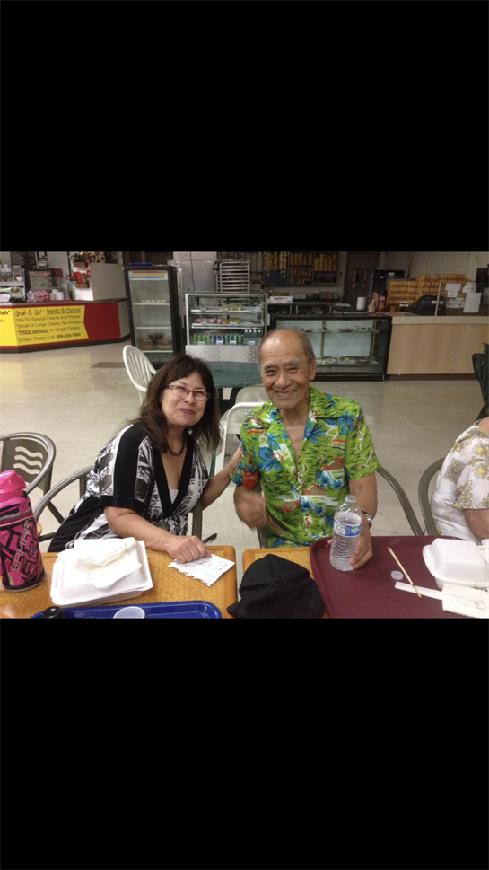 Two friends smile and pose while sharing a meal at a community center, surrounded by casual decor.