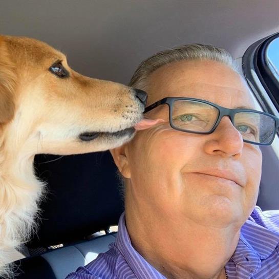 A man smiles as his dog gives him a friendly kiss while they are in a car.