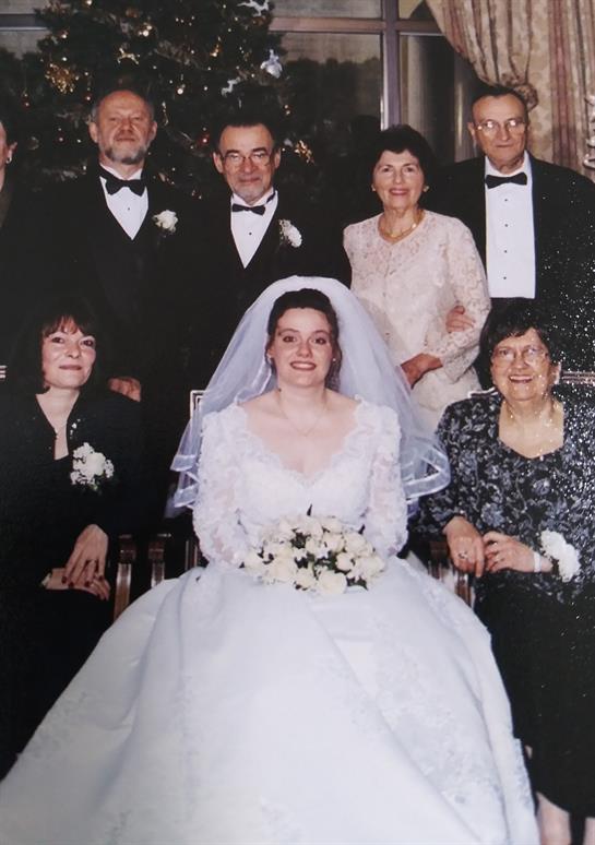 A joyful bride in a white gown sits in front of her family and friends at a wedding ceremony.