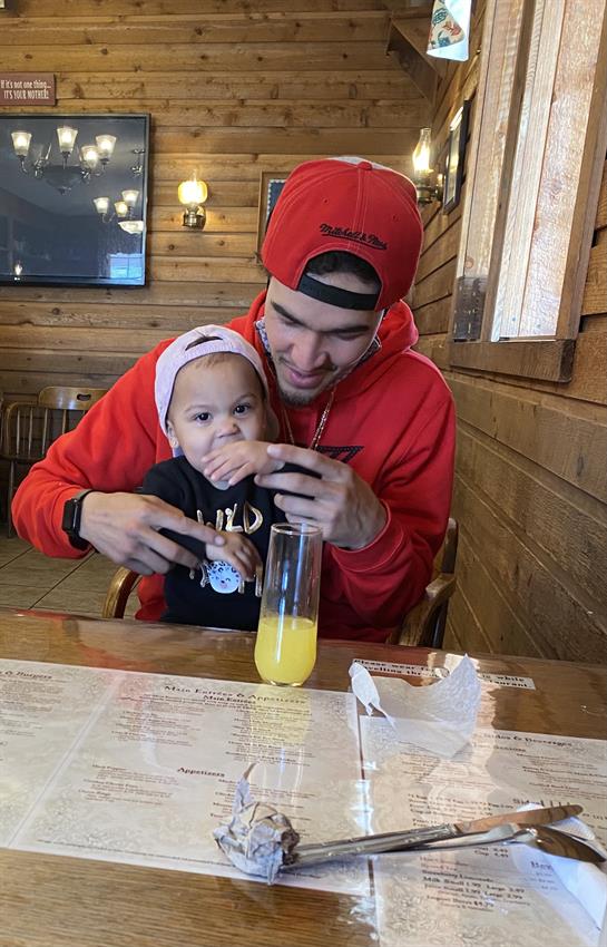 A joyful father plays with his young child at a wooden restaurant table, sharing a drink.