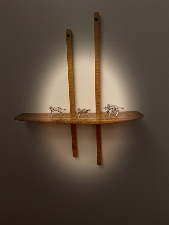 Metal sculptures of animals are arranged on a wooden shelf illuminated by warm light in a cozy room.