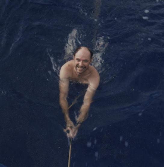 A man swims energetically in deep blue water, laughing while holding a rope in the ocean.