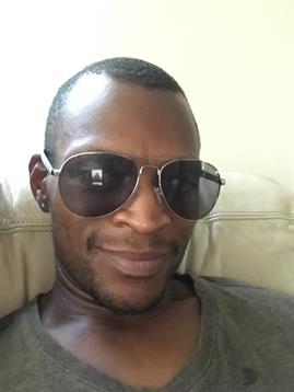 A man wearing sunglasses smiles while lounging comfortably on a couch at home.