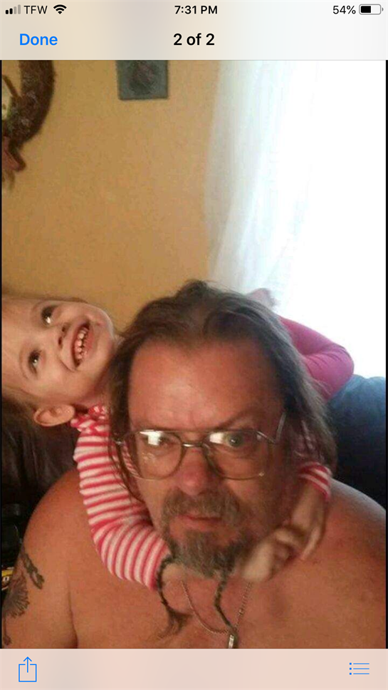 A grandfather has a playful expression as his granddaughter hugs him from behind.