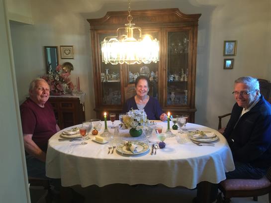 Three people enjoy dinner at a beautifully arranged table with candles and decor in a warm setting.