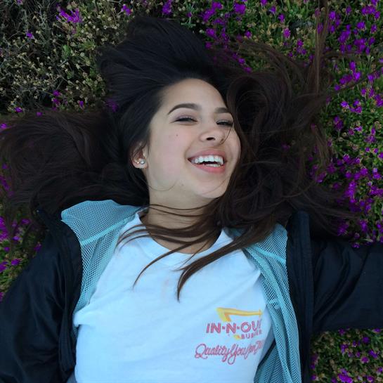 Woman lies on the ground, smiling while surrounded by vibrant purple flowers and greenery.
