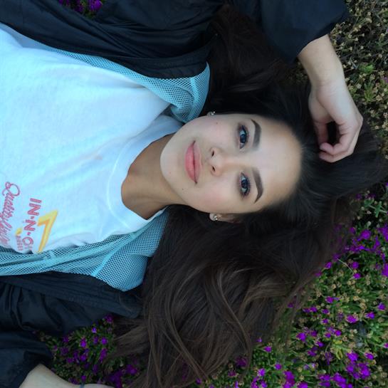 Woman lies on grass among purple flowers, enjoying the sunny afternoon in a peaceful garden.