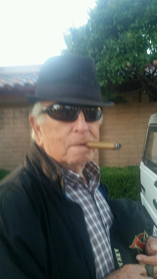 Man with sunglasses and a hat smokes a cigar while standing in front of a vehicle.