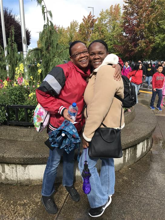 Two friends smile while posing for a picture at a vibrant gathering with flowers surrounding them.