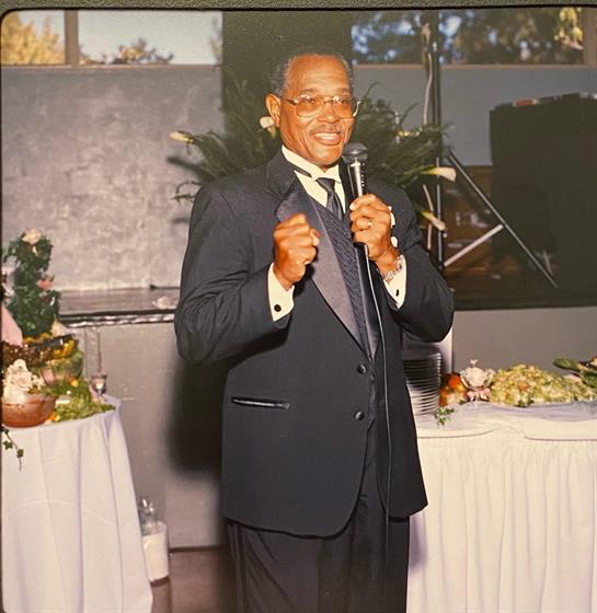 An elderly gentleman speaks confidently at a formal gathering featuring elegantly set tables.