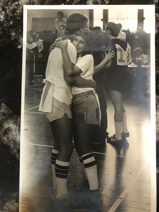 Two couples share a joyful moment while dancing together in a sports hall at dusk.