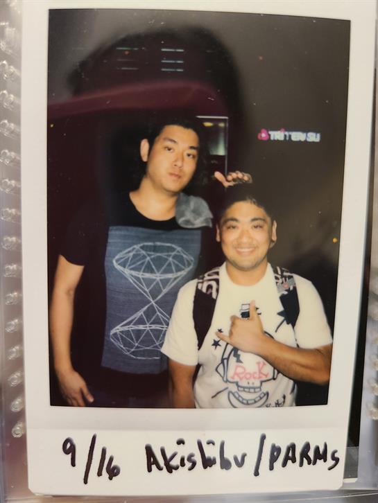 Two friends smile while standing close together under colorful lights in the city.