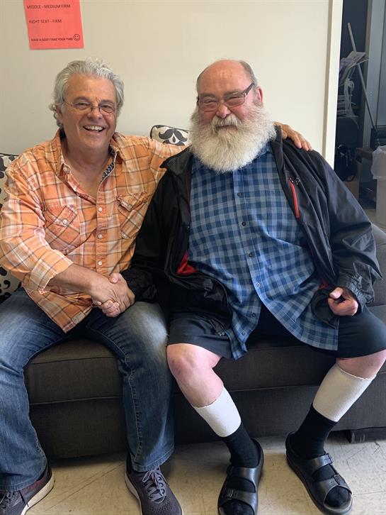 Two men are happily shaking hands while sitting comfortably on a couch in a cozy living room.