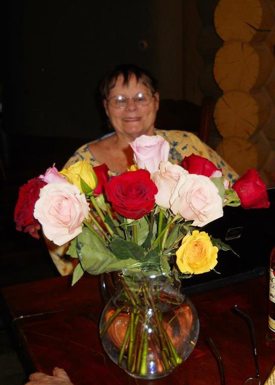 A joyful elderly woman poses with a colorful bouquet of roses in a warm, inviting space.