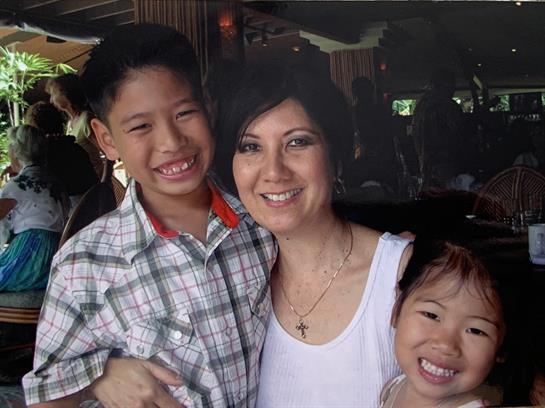 A woman stands happily with two children, surrounded by a lively crowd at a community event.