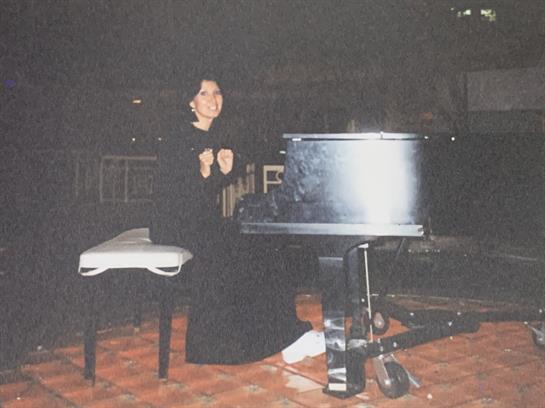 A musician wearing a dark outfit passionately plays a piano in an intimate setting.
