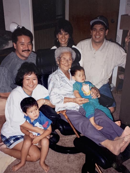 Relatives of various ages sit together smiling in a warm family gathering setting.