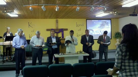 Men are gathered inside a church, participating in a religious service with readings and prayer.