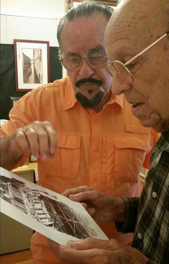 Two men intensely examine vintage photographs, sharing stories in a cozy art gallery.