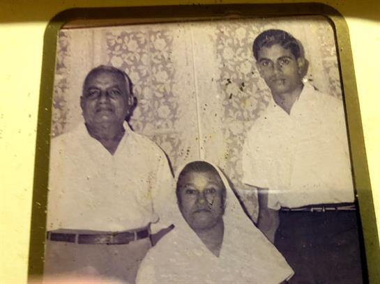 Three people in traditional clothing smile together by textured curtains.