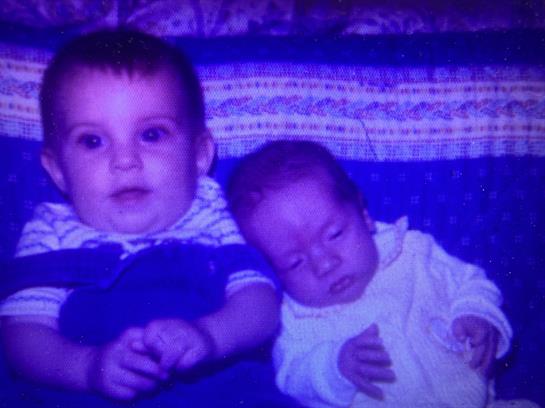 Two children lounge on a blue blanket, one sleeping, the other curiously gazing.