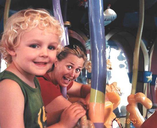 A child smiles while interacting with vibrant ride elements alongside an excited adult.