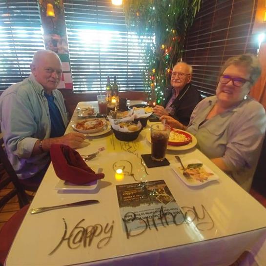 Three friends enjoy a birthday dinner at a cozy restaurant, with festive decorations on the table.