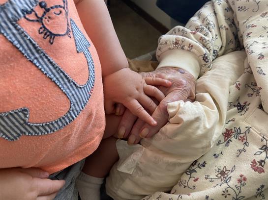 A child gently holds hands with an elderly person, showcasing a loving connection.