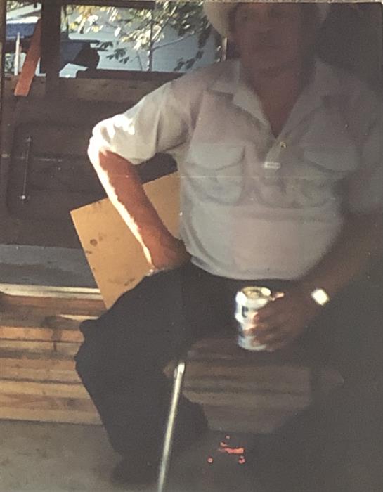 A man relaxes with a drink in hand, enjoying the warm sunlight outside near wooden structures.