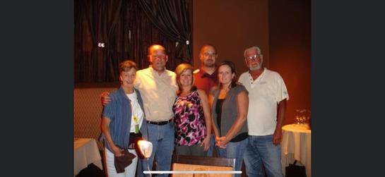 Six people smiling together at a restaurant, enjoying good company and conversation.