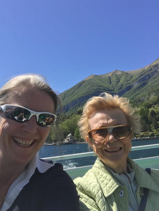 Women share a joyful moment on a boat surrounded by scenic mountains and clear blue skies.