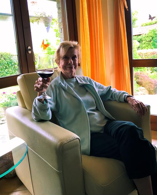 A woman relaxes in her chair, sipping wine while enjoying the sunny view from her home.