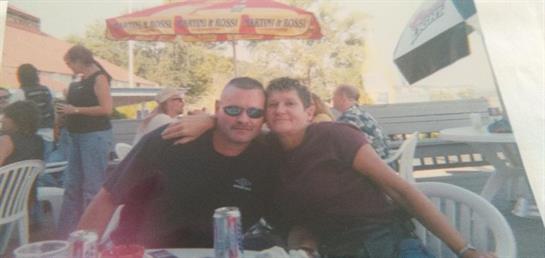 Couple smiles together at a lively outdoor event while friends socialize nearby.