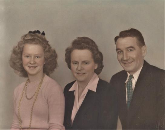 Three adults smile for a portrait in a studio, showcasing vintage fashion styles and hairstyles.