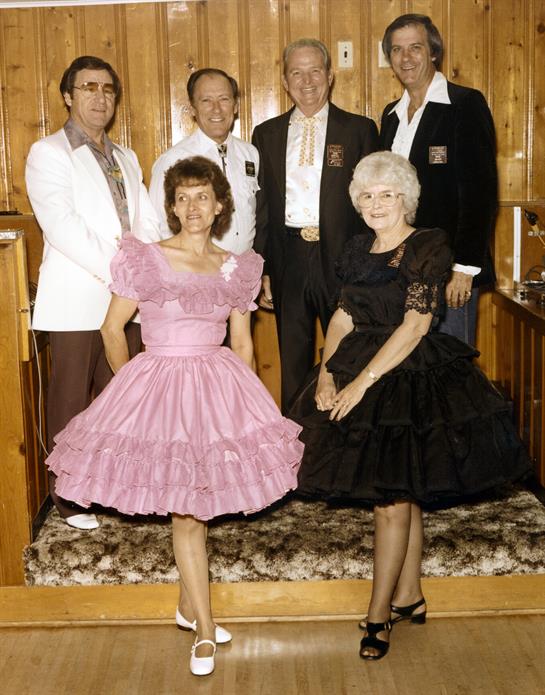 A diverse group of six in colorful formal attire poses, highlighting vintage fashion.