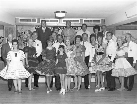 Participants in vibrant dresses gather for a joyful dance at a cultural celebration indoors.