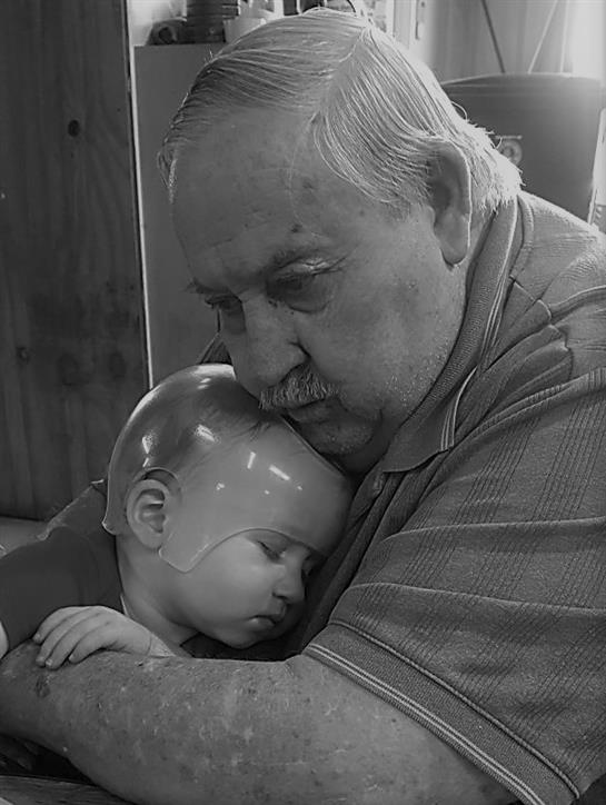 An elderly man gently holds a sleeping infant, showing warmth and connection.