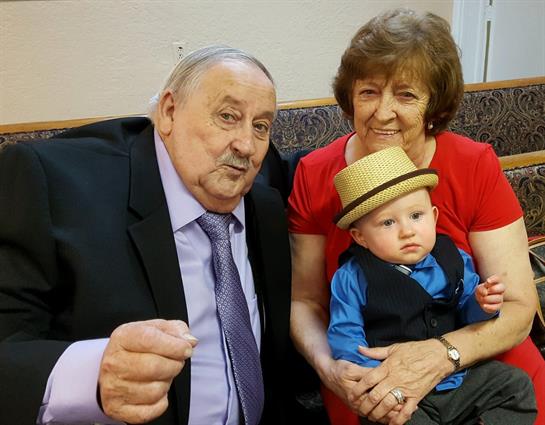 Grandparents proudly pose with their grandson in a suit and hat at a joyful celebration.