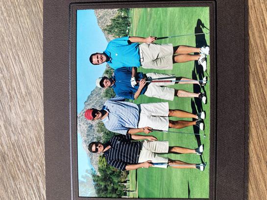 Four friends pose with golf clubs on a green course surrounded by mountains.