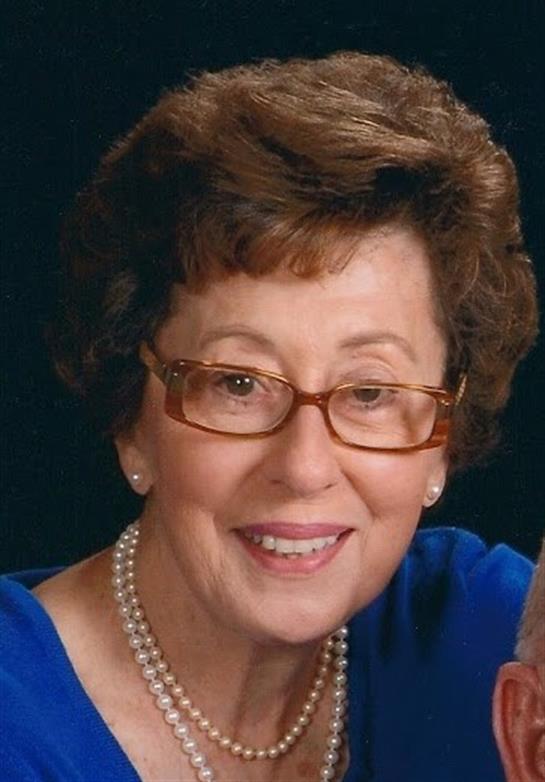 Woman in blue top smiles warmly, exuding friendliness and positivity in a close-up shot.