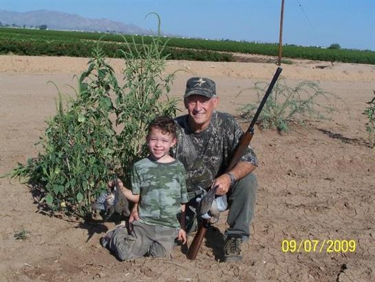 A man and a boy proudly display their hunting prize while surrounded by nature in the countryside.