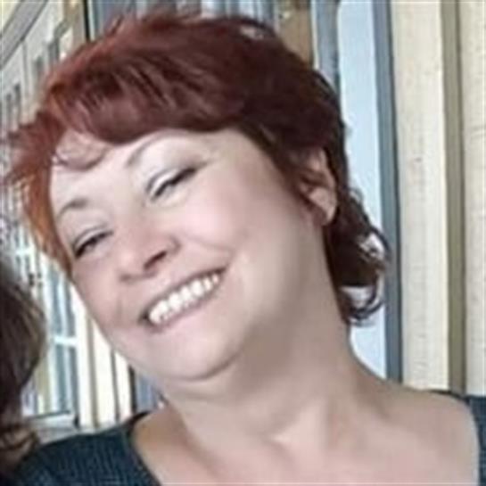 A woman with red hair smiles brightly in a cozy indoor space during a friendly gathering.