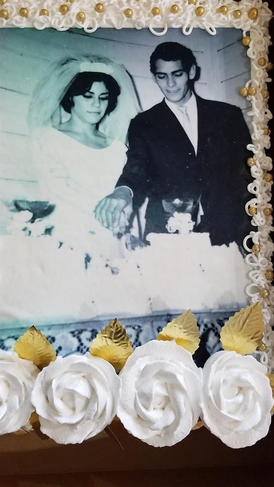 A newlywed couple stands by a beautifully decorated wedding cake adorned with white roses.