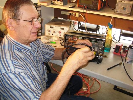 A technician works diligently on electronic equipment with tools laid out in a busy workshop.
