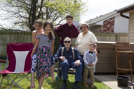 Group of family members gathers in a backyard, enjoying a sunny day, creating memories together.