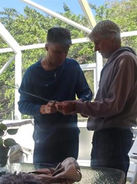Two individuals focus on assembling fishing rods outdoors under a bright sky.